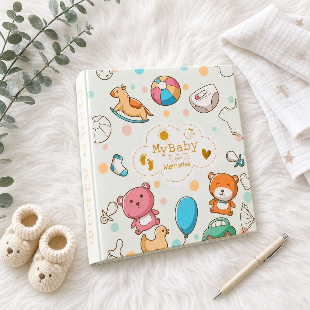 Kiddospot baby memory book with a colorful cartoon cover design, styled in a flat-lay on a white faux fur surface with a cream pen, a white muslin cloth, and a small knit baby bootie prop.