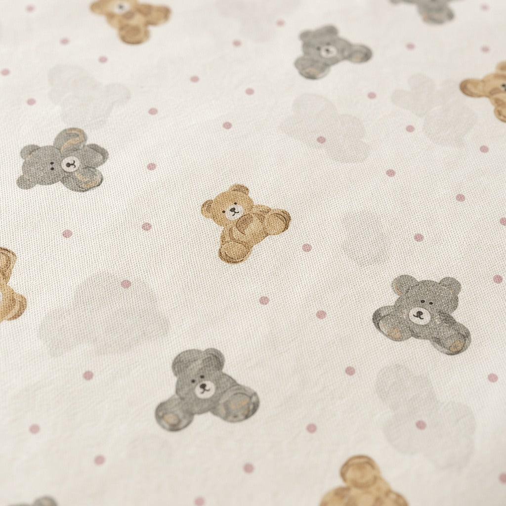 Close-up of a fabric surface with a repeating pattern of teddy bears in tan and gray, small gray clouds, and pink polka dots on a warm off-white background.
