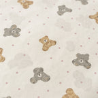 Close-up of a fabric surface with a repeating pattern of teddy bears in tan and gray, small gray clouds, and pink polka dots on a warm off-white background.