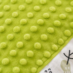 Close-up of a Kiddospot's bright lime green baby blanket or swaddle featuring a raised dotted tactile pattern, with a corner showing a white printed fabric section with a cartoon character.