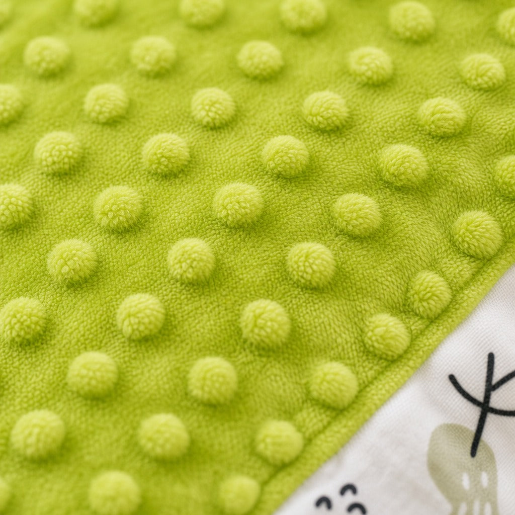 Close-up of a Kiddospot's bright lime green baby blanket or swaddle featuring a raised dotted tactile pattern, with a corner showing a white printed fabric section with a cartoon character.