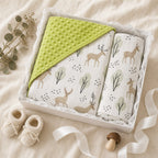 A baby gift set in a white box containing a Kiddospot lime green minky dot blanket and a pair of deer-patterned muslin blankets, styled on a beige fabric background with baby booties, a mushroom, and eucalyptus.