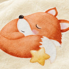 Close-up of a soft cream-colored textile featuring a sleeping orange fox illustration with a yellow star accent.
