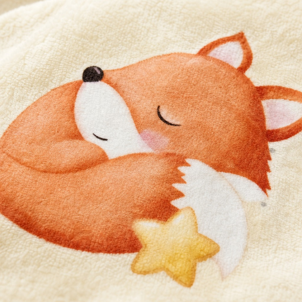Close-up of a soft cream-colored textile featuring a sleeping orange fox illustration with a yellow star accent.
