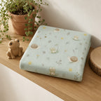 A folded light blue Kiddospot fitted sheet with a whimsical frog, snail, and dandelion print, styled on a wooden shelf next to a small frog figurine and a potted trailing plant.
