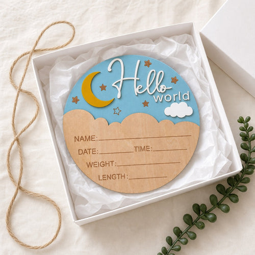 Kiddospot Hello World baby announcement sign propped on white nursery shelf with succulent pot and folded muslin cloth