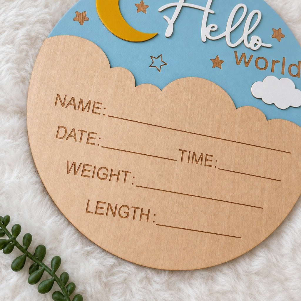 A round wooden baby milestone plaque with a light blue sky design, featuring a yellow crescent moon, white clouds, and the words 'Hello world'. The front has engraved lines for writing baby's name, date, time, weight, and length.