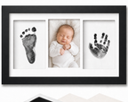 Newborn inkless print kit with black frame and white mat, showing handprint and footprint impression cards on a white background