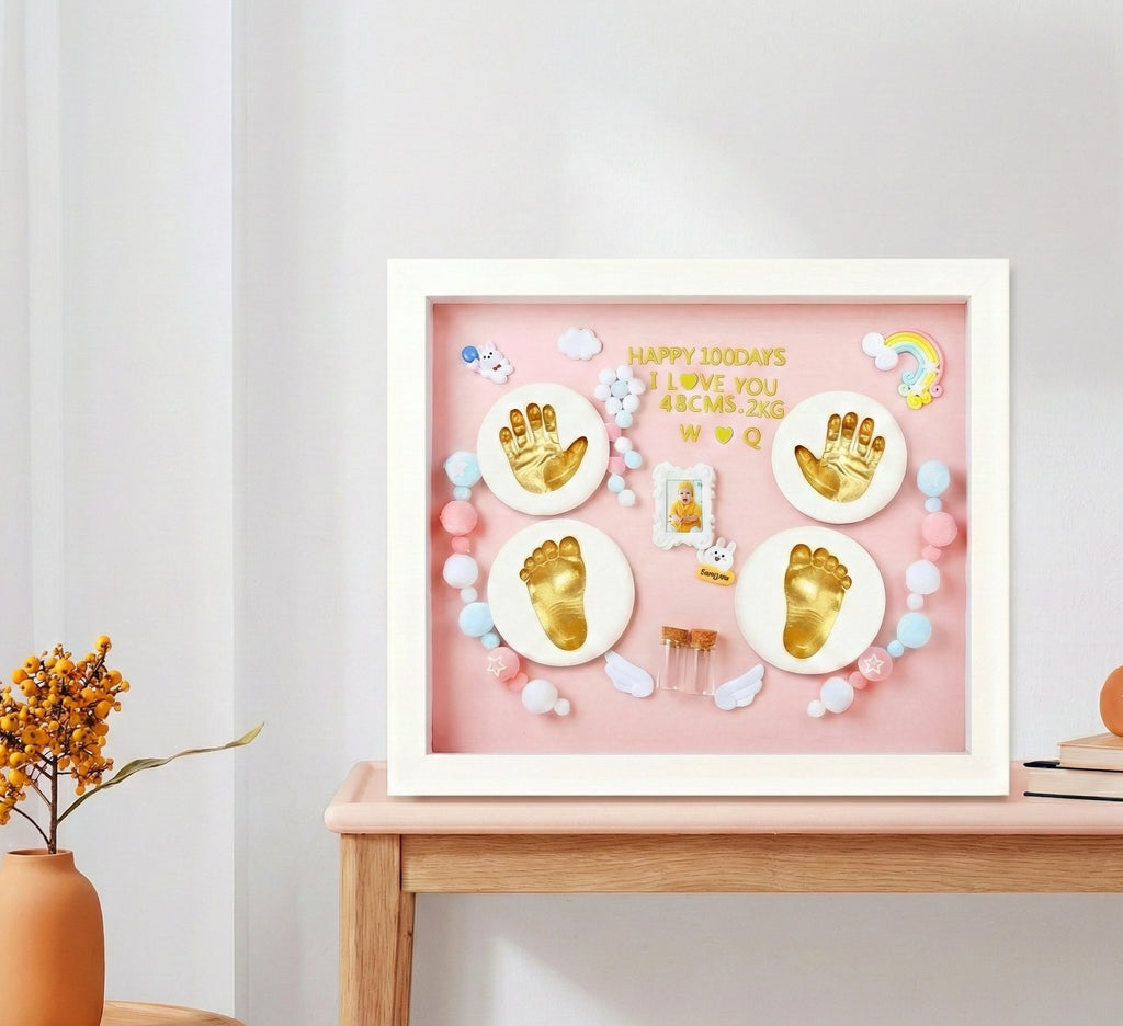 Decorative shadow box with gold hand and footprints on a pink background, placed on a wooden surface.