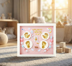 Decorative shadow box with gold hand and footprints, colorful beads, and baby-themed elements on a pink background.
