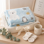 Kiddospot blue baby blanket with polar bear and penguin design, socks, and a mug on a wooden surface.