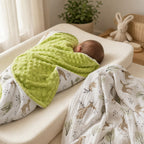 Newborn baby snuggled in the Kiddospot Deer Minky Blanket showing the lime green dimple bubble reverse side, with the woodland deer print front and matching muslin swaddle visible nearby. Cosy warm nursery lifestyle photography.