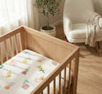 Wooden crib with floral bedding in a room with a chair and plant