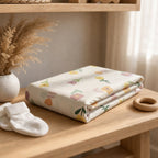 Kiddospot floral-patterned baby cot fitted sheet on a wooden surface with white socks and a small wooden item.
