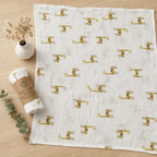 Kiddospot GOTS Organic Muslin Swaddle in Giraffe Print pattern on a wooden surface with rolled-up swaddle and vase.