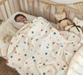 Newborn baby in a crib with a colorful heart-patterned blanket and teddy bears.