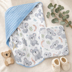 Overhead flat lay of the Kiddospot Koala Minky Blanket and Muslin Swaddle Set — both matching Australian koala print pieces shown with sky blue dimple reverse visible, styled with eucalyptus, a wooden koala figurine and cream knitted booties. Iconic Australian baby shower gift.