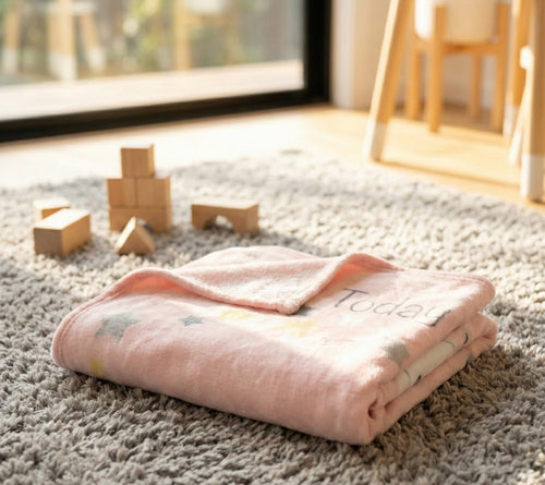 Pink blanket with star patterns on a carpeted floor with wooden blocks