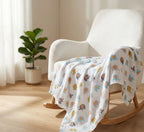 Rocking chair with a colorful baby blanket draped over it in a room with a plant and curtains.