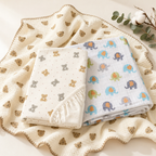 Kiddospot Organic Nursery Starter Bundle — GOTS certified organic cotton baby blanket, elephant print muslin swaddle, and bear cot fitted sheet flat-lay