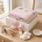 Kiddospot pink baby milestone blanket with star patterns on a white box, accompanied by baby socks and a small dish on a wooden surface.