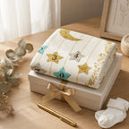 Kiddospot folded baby milestone white blanket with numbers and stars on a white box with a gold ribbon, next to baby socks and a pen on a wooden surface.