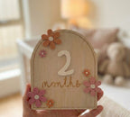 Kiddospot wooden baby milestone card held in hand showing 2 months — natural wood detail
