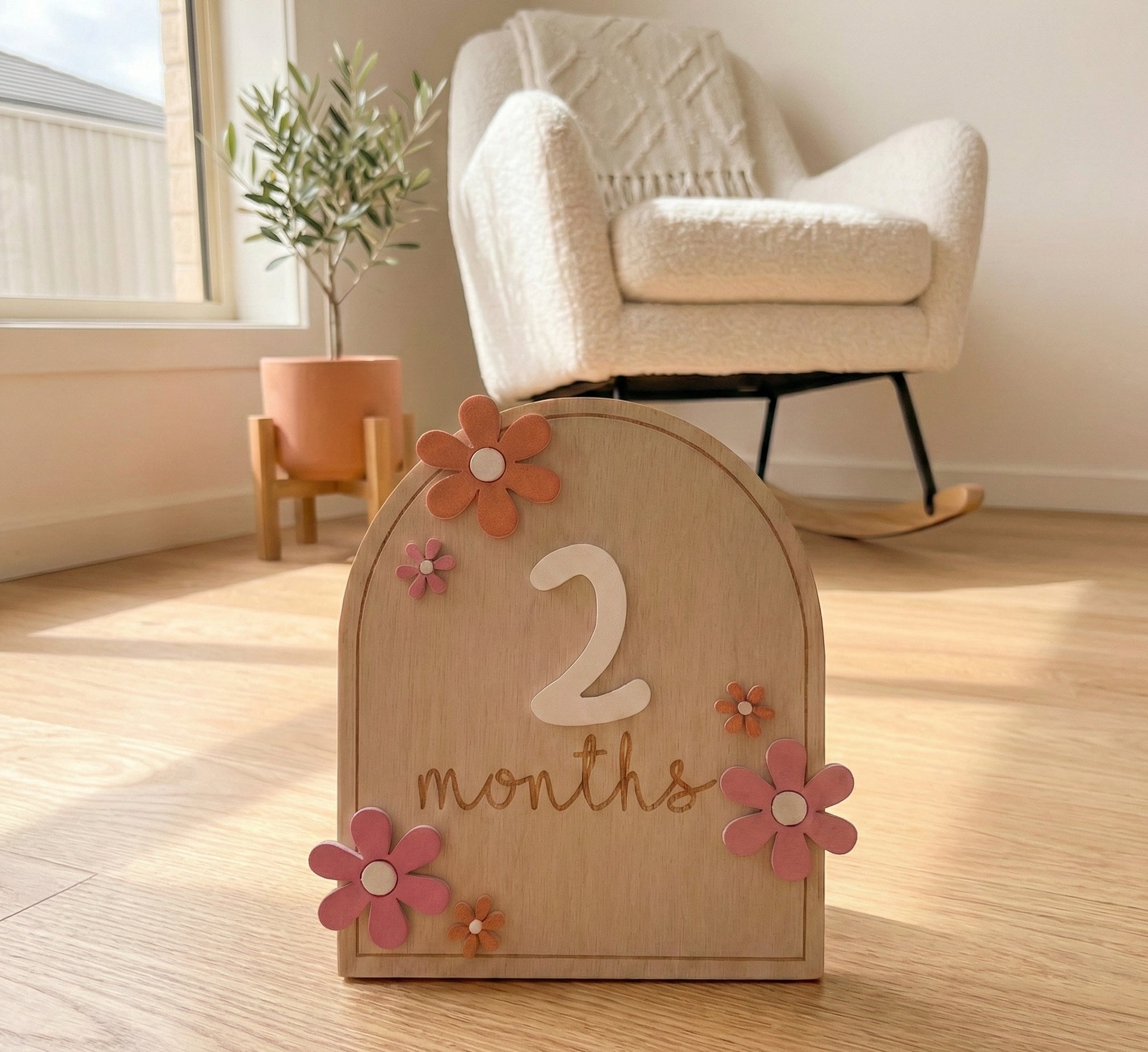 Wooden plaque with '2 months' and decorative flowers on a wooden floor.
