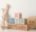 Stack of wooden blocks with engraved text next to a plush bunny toy on a light background