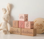 Stack of wooden blocks with milestone text next to a plush bunny toy on a light background