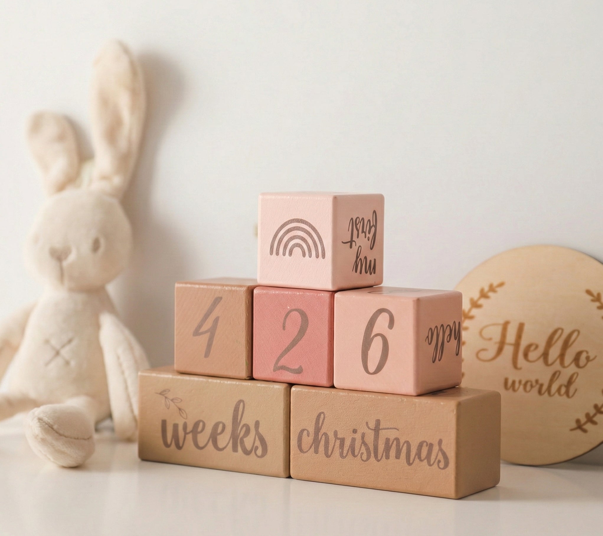 Stack of wooden blocks with milestone text next to a plush bunny toy on a light background