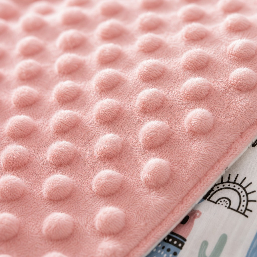 Close-up of a Kiddospot soft pink baby blanket with a raised circular tufted texture, folded over to reveal a printed white fabric underside with a sun and cactus design.