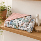 A folded minky Kiddospot blanket and matching pillowcase with a whimsical desert animal print, styled on a wooden shelf next to a potted plant and a white llama figurine.