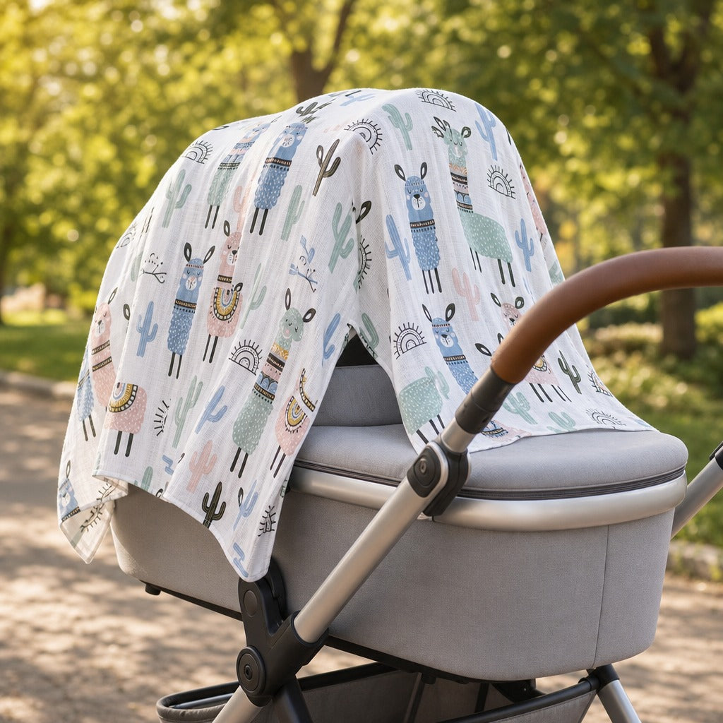 A Kiddospot white muslin baby stroller canopy cover with a colorful llama and cactus pattern, draped over a gray stroller in an outdoor park setting.