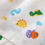 Close-up of a Kiddospot white muslin fabric with a colorful dinosaur print, including yellow, green, blue, orange, and purple dinosaurs.