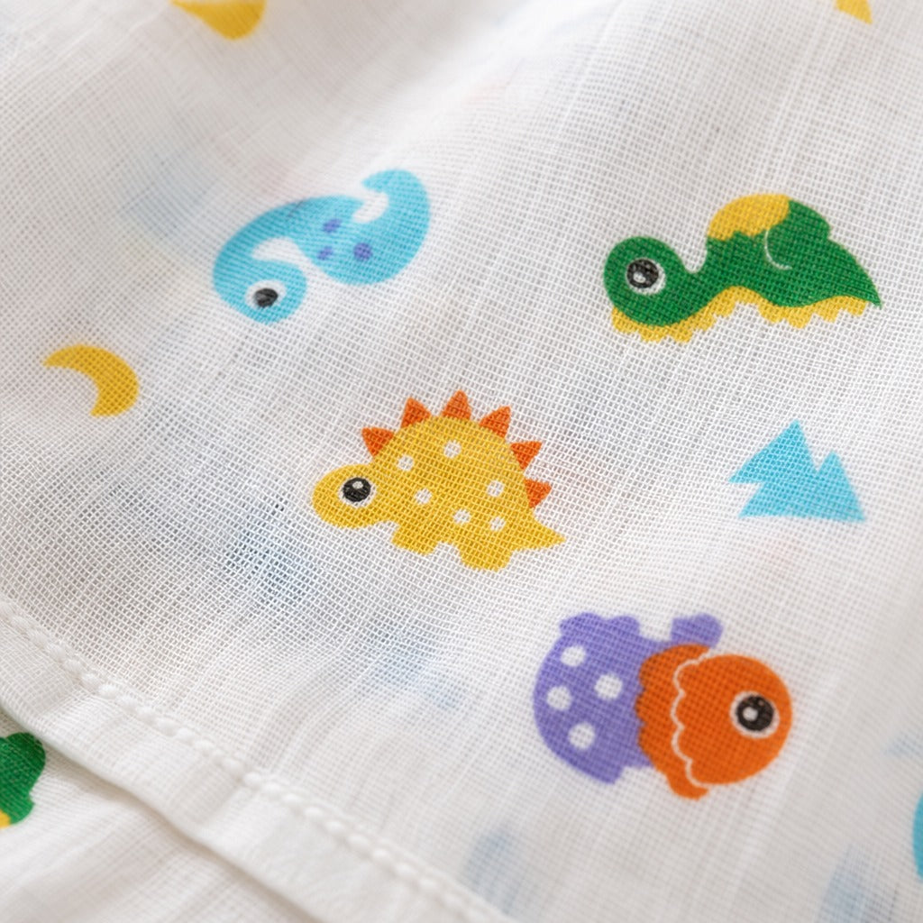 Close-up of a Kiddospot white muslin fabric with a colorful dinosaur print, including yellow, green, blue, orange, and purple dinosaurs.
