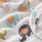 Close-up of a white Kiddospot muslin blanket with a playful elephant print featuring light blue, dark navy, pink, gray, and olive green elephants with orange chevron-patterned trunks.