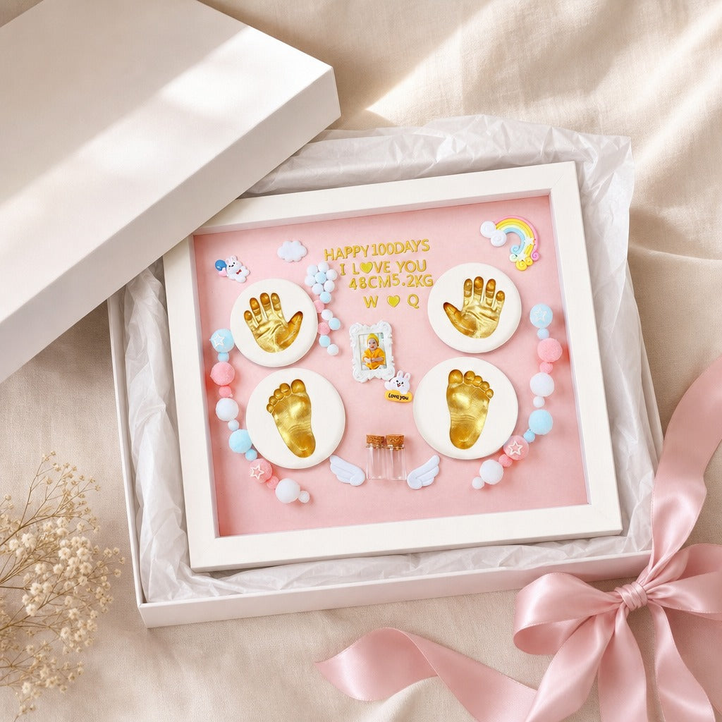 Kiddospot baby keepsake framed shadow box gift set displayed in an open white box with a pink insert. The frame contains gold baby foot and handprints, white circular bases, pastel beads, small angel wings, and the text 'HAPPY 100 DAYS I LOVE YOU ABCMS-2165 W 19 Q' on a soft pink background.