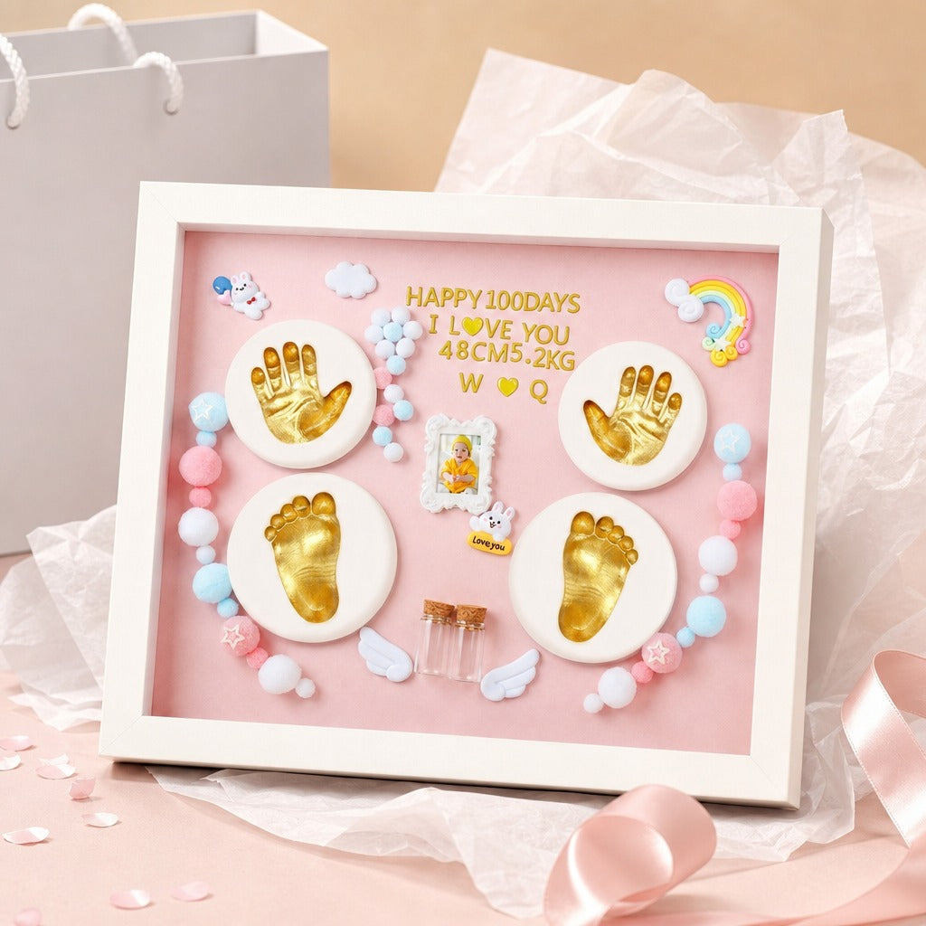 Kiddospot framed baby keepsake display with a white frame and pink backing, featuring gold footprints and handprints, pastel beads, small wings, a tiny photo frame, and gold lettering that reads 'HAPPY 100DAYS I LOVE YOU 48CM.5.