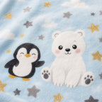 A folded light blue blanket with a white polar bear illustration and gray and yellow stars, displayed on a wooden bench in a styled nursery-like setting with a basket, plush toy, block, and dried grass in a vase.