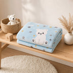 A folded light blue blanket with a white polar bear illustration and gray and yellow stars, displayed on a wooden bench in a styled nursery-like setting with a basket, plush toy, block, and dried grass in a vase.
