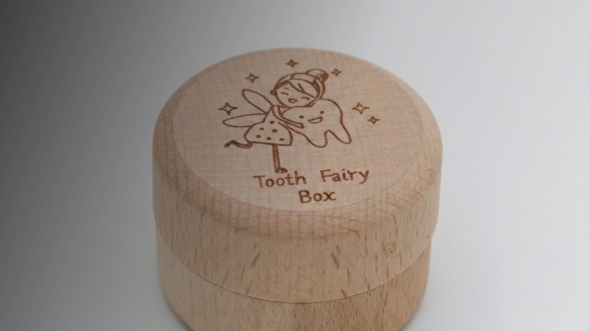 Kiddospot Wooden Tooth Fairy Box Classic — small cylindrical solid beechwood screw-top box approximately 38–45mm diameter with a laser-engraved whimsical tooth fairy illustration hugging a smiling tooth, surrounded by twinkling stars, and "Tooth Fairy Box" in cursive script on the lid. Natural matte finish. Roomy interior holds all 20 baby teeth. Childhood keepsake for ages 5 and up. Not a toy — a meaningful gift from parents, grandparents and gift givers. Free AU shipping. kiddospot.com
