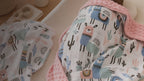 Kiddospot Llama Minky Baby Blanket and Muslin Swaddle Set — two-piece matching newborn gift set featuring a playful llama and cactus print on white, with colourful llamas in dusty blue, sage green and dusty pink wearing tribal saddles. Ultra-plush salmon-pink dimple minky blanket reverse plus lightweight breathable muslin swaddle. Standout baby shower gift. Free AU shipping. kiddospot.com