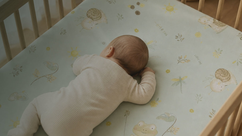 Kiddospot GOTS Organic Cotton Cot Fitted Sheet in Frog and Snail design — pale mint green base with watercolour-style frogs on lily pads, cream snails with swirly shells, light blue dragonflies, yellow suns and botanical sprigs. 132x72cm, deep elastic pockets, fits standard cot mattresses. 100% breathable woven cotton, machine washable. Whimsical gender-neutral nursery design. Free AU shipping. kiddospot.com