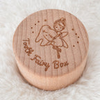 Kiddospot round wooden keepsake box lid engraved with a fairy holding a bell and the words 'Fairy Box,' placed on a soft white faux-fur surface.