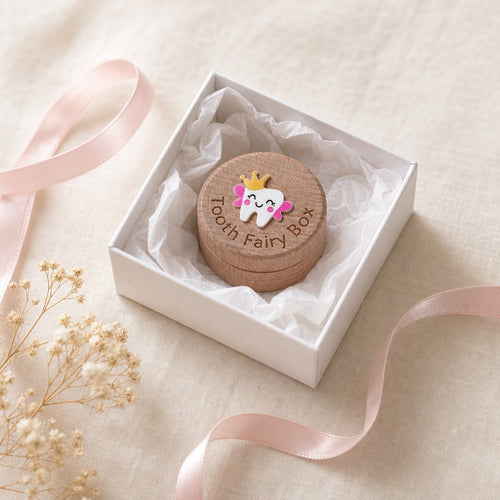 Kiddospot round wooden keepsake box labeled 'Tooth Fairy Box' with a small tooth charm decorated with a crown and pink wings, presented in a white gift box on a beige fabric background with a pink ribbon.
